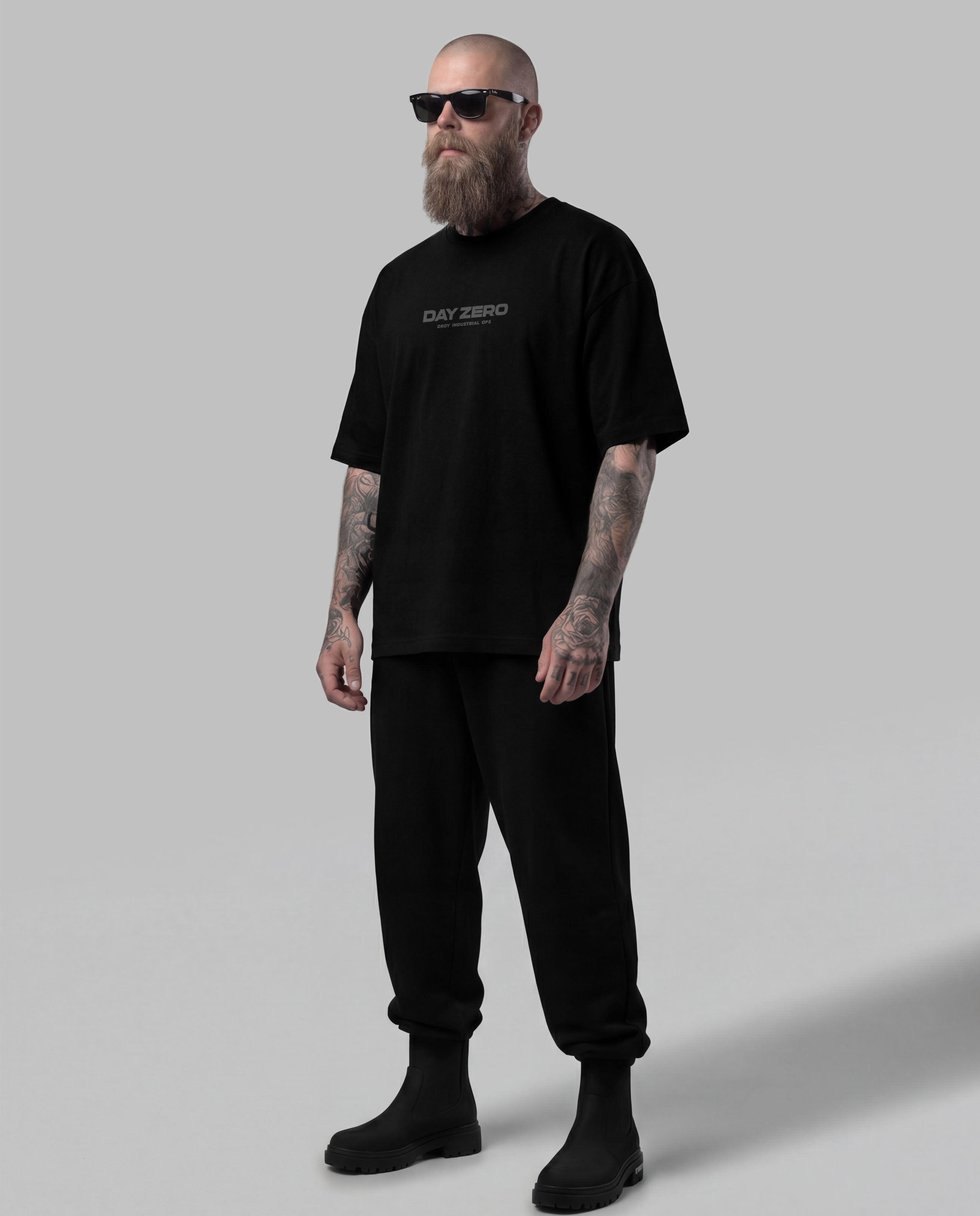 Man wearing a black t-shirt with text and black pants on a gray background