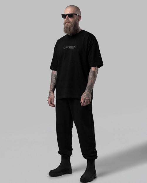 Man wearing a black t-shirt with text and black pants on a gray background