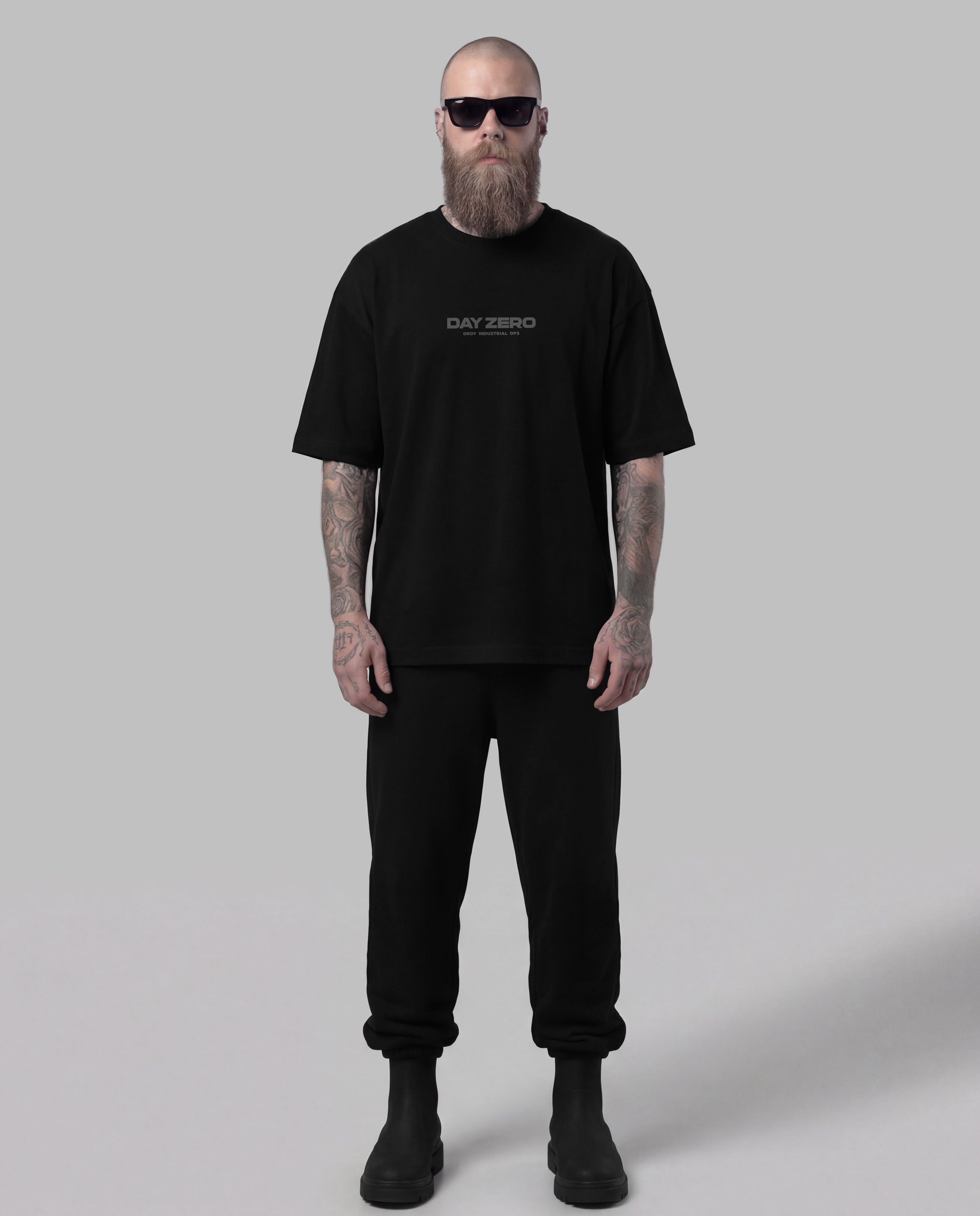 Man wearing a black t-shirt and pants with sunglasses on a gray background