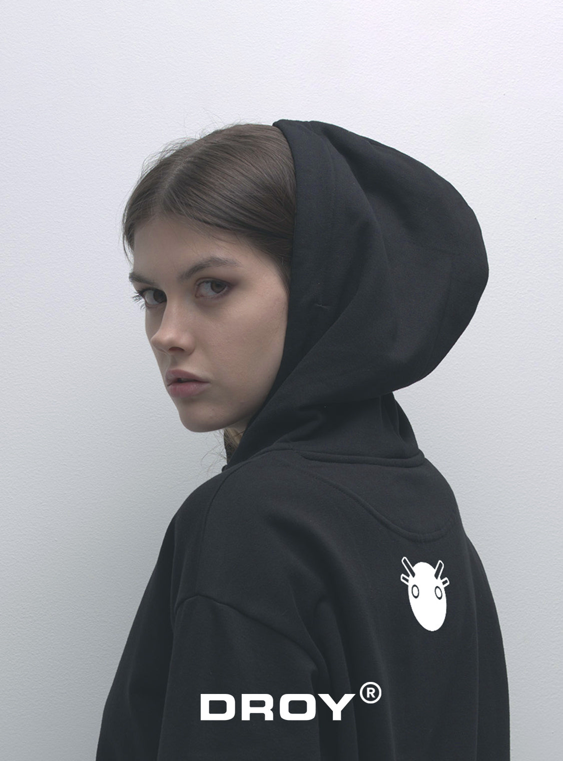 Person wearing a black hoodie with 'DROY' logo on the back against a white background