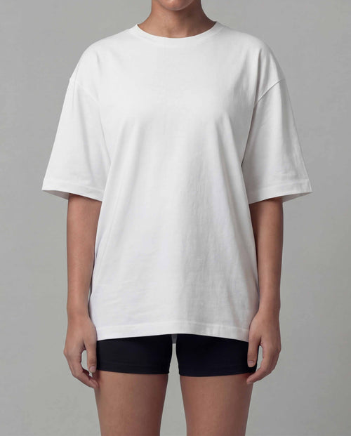 Person wearing a loose-fitting white t-shirt and black shorts on a gray background