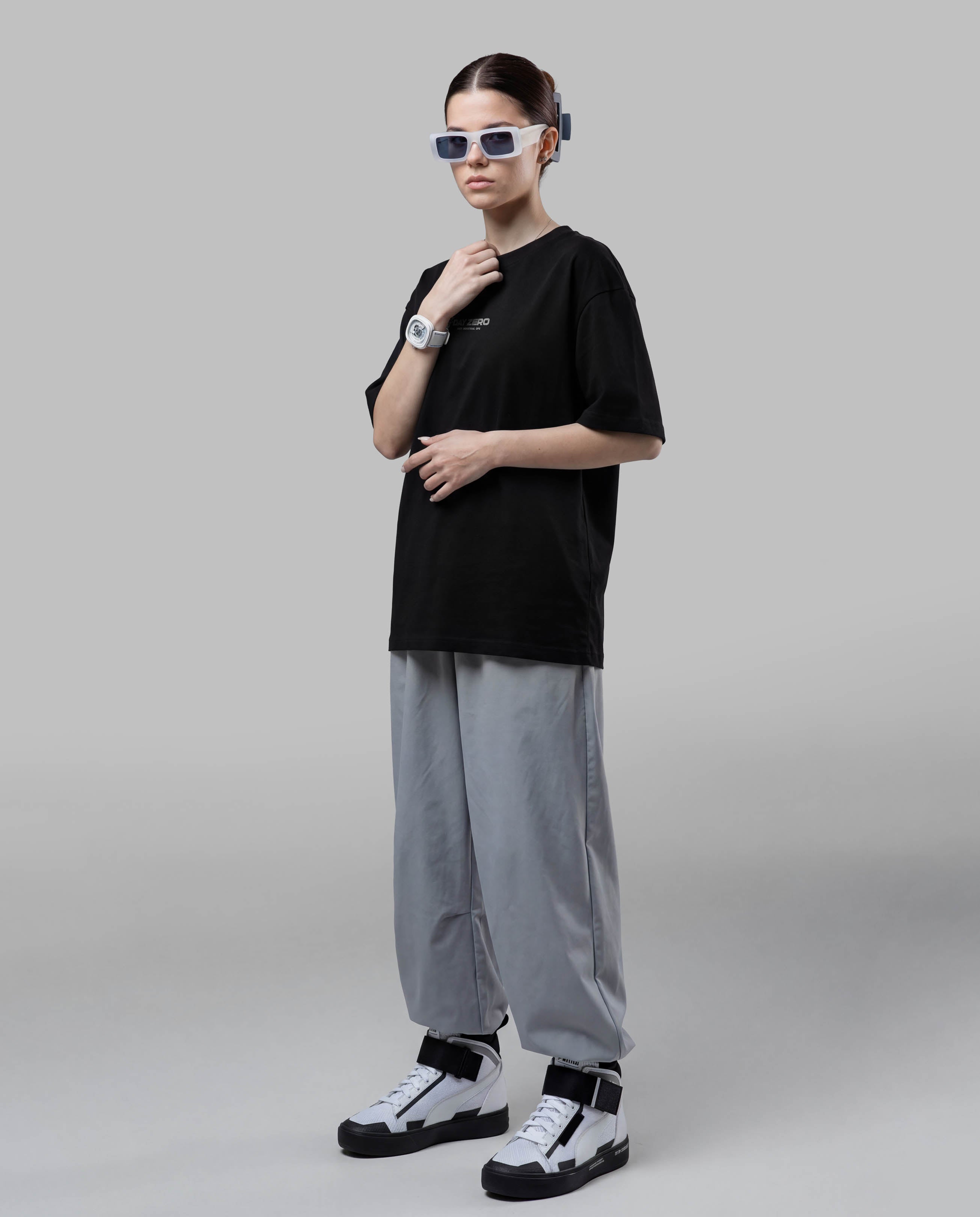 Person wearing a black t-shirt, gray pants, and white sneakers on a plain background