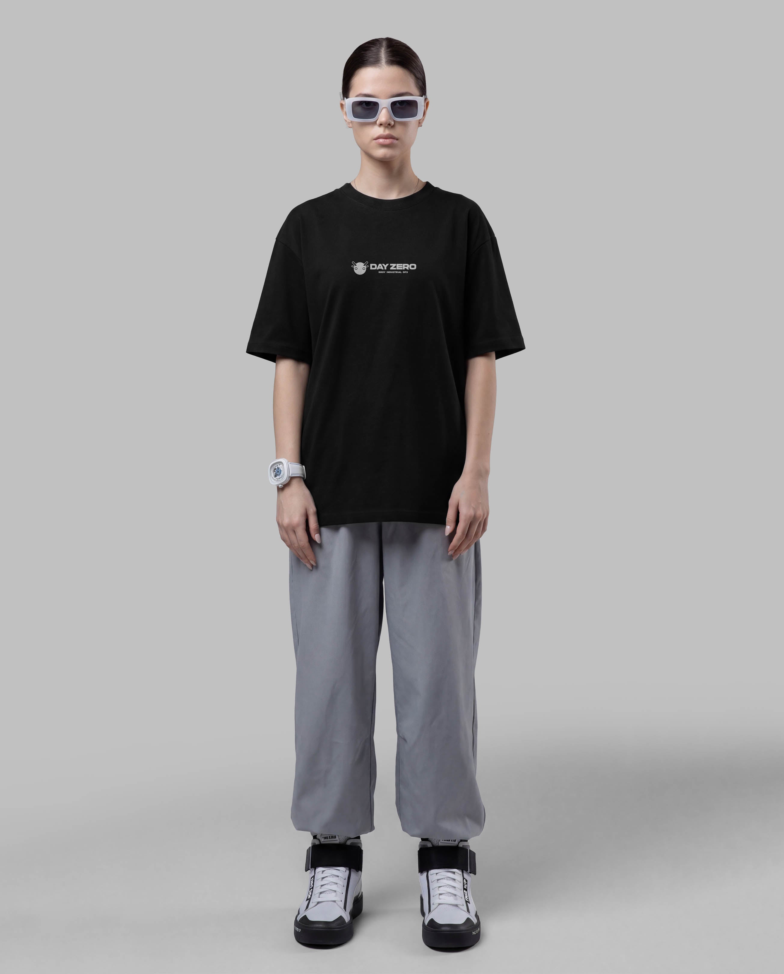 Person wearing a black t-shirt with a logo and gray pants on a plain background